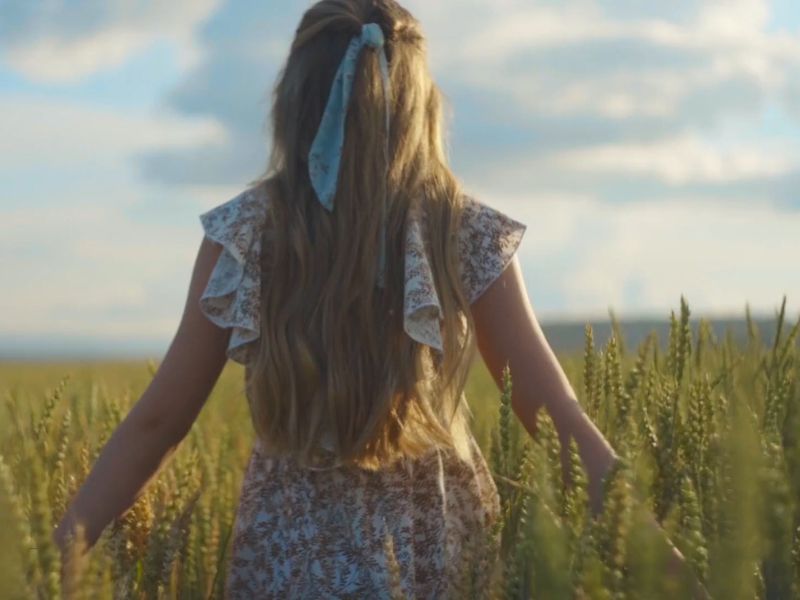 devojka sa dugom kosom i maramom u njoj šeta kroz polje pšenice